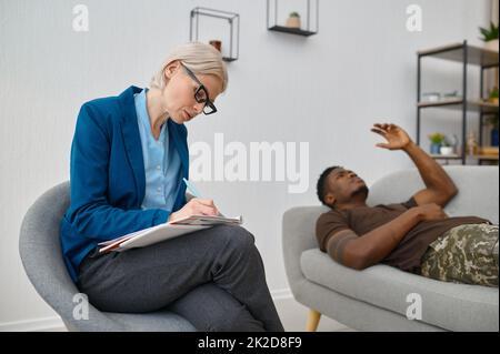 Psychologist making notes while male soldier talking Stock Photo