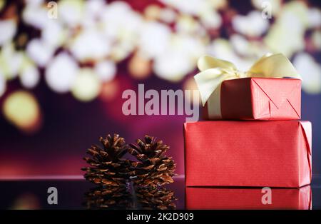 Christmas is here. Shot of Christmas gifts and pine cones on a table with Christmas lights in the background. Stock Photo