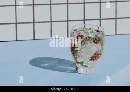 Cocktail with berries and ice on a white tile and blue table background. Front view. Stock Photo