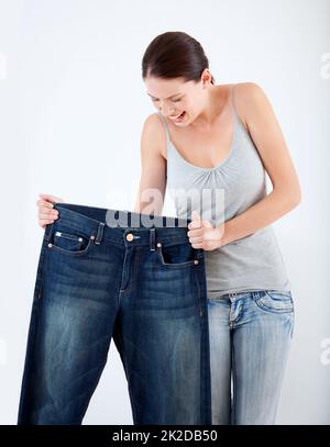 Ive come so far. A pretty, slim woman holding up a pair of her old oversized jeans. Stock Photo