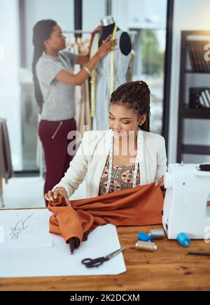 Doing their jobs perfectly. Shot of a young fashion designer sewing garments while a colleague works on a mannequin in the background. Stock Photo