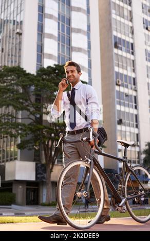 Ill be at the office in 10. a businessman taking a phone call while commuting to work with his bicycle. Stock Photo