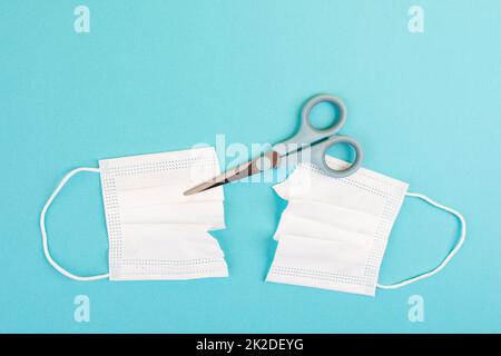 Covid-19 mask cut into two pieces with a scissor, end of pandemic, back to normal, epidemic Stock Photo