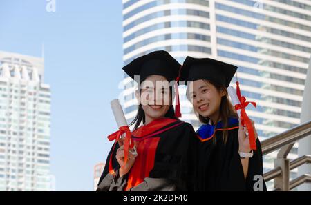 Two graduated women friends holding diplomas in hands and celebrating their success with smiles. Stock Photo
