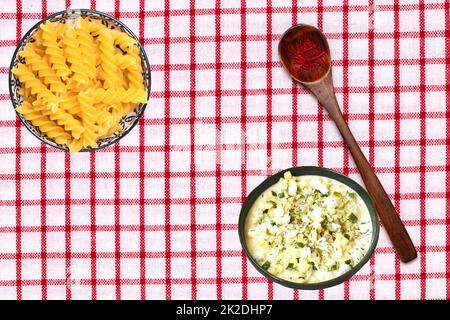 Vegetable food. Closeup of two bowls with noodles and greek soup and a spoon with safran spice threads on a tablecloth. Healthy eating and nutrition. Top view with space. Stock Photo