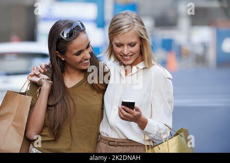 Girls day out. Two young women standing outside with shopping bags sending a text message. Stock Photo