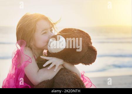 The innocence of childhood. Portrait of a cute little girl playing with her teddy bear on the beach.