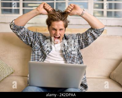When technology fails, anger ensues. A young man looking frustrated while working on his laptop. Stock Photo