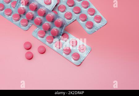 Top view pink tablet pills and blister pack of pills on pink background. Prescription drug. Vitamins, minerals, and supplements. Pharmaceutical industry. Health care and medicine. Pharmacy product. Stock Photo