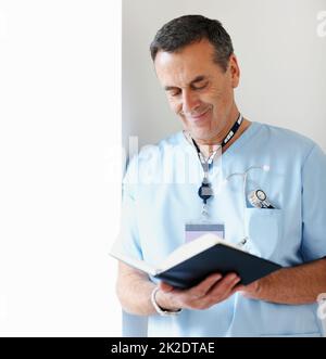 Happy medical doctor noting schedule while leaning against wall. Portrait of a smiling medical doctor noting schedule while leaning against wall. Stock Photo