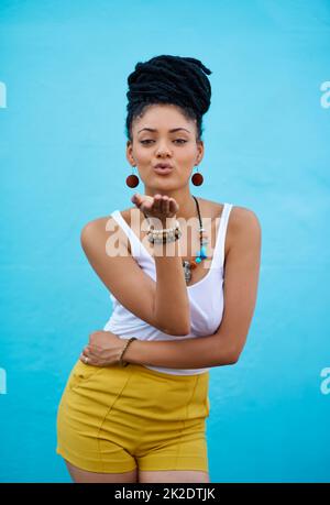 Sending you sweet love. Portrait of a trendy young woman blowing kisses against a blue background. Stock Photo