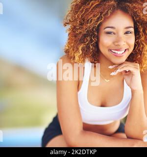 Happy african american brunette sporty girl with dreadlocks and good  figure, sit at home on fitness mat, watching online fitness video lessons on  laptop, care her health, looks at the camera, smiling