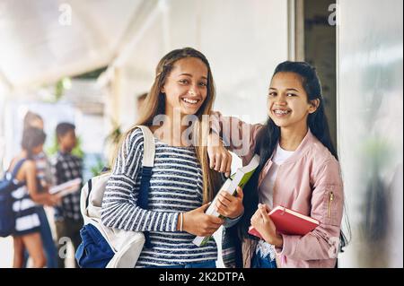 Best friends and study buddies. Portrait of two happy schoolgirls standing together in the hallway outside their classroom. Stock Photo