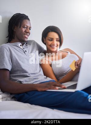 Spoil her in the bedroom. Shot of a young couple doing some online shopping with a credit card. Stock Photo