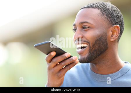Happy man with black skin dictating text on cell phone Stock Photo