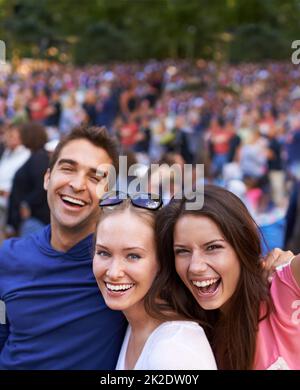 Nothings better than a festival with friends. A group of smiling friends standing together at a music festival with crowd in the background. Stock Photo