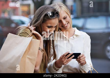 Save those directions. Two young women standing outside with shopping bags sending a text message. Stock Photo