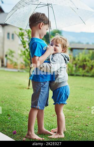 Well stay dry under this umbrella. Shot of a cheerful little boy and girl standing together under an umbrella outside during a rainy day. Stock Photo