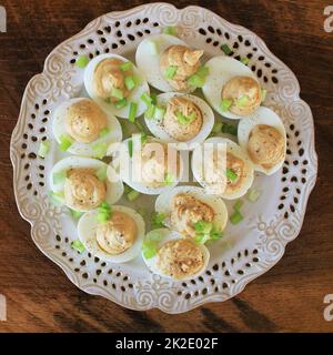 Deviled eggs with cod livers with leek on white plate. Rustic wooden table Stock Photo
