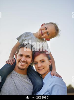 Enjoying a family day outdoors. Portrait of smiling mother and father carrying there little boy on their shoulders outside. Stock Photo