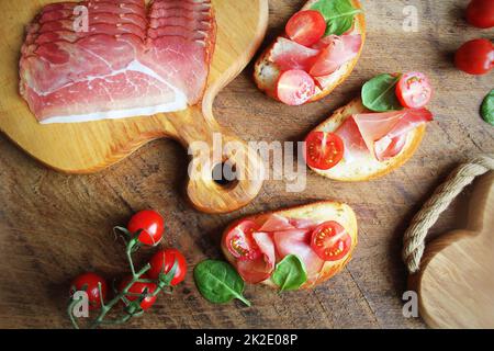 Bruschetta with prosciutto ham, cherry tomatoes and green spinach . Top view Stock Photo