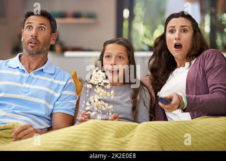 They love scary movies. Shot of a family sitting on their living room sofa watching a movie and eating popcorn. Stock Photo