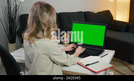 Blonde business woman sitting with her back in the gray jacket typing on the computer Stock Photo