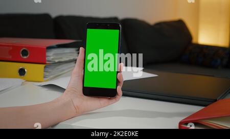 Woman at home relaxing reading on the smartphone with pre-keyed green screen, Chromakey Mockup. Stock Photo