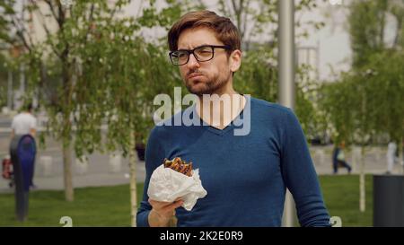 Busy Business man Lunch Eating snack. Employee Taking Break Work. Eat Snack walking .Cheerful Business man Having Lunch Break Outdoor. Hungry Man Eat. Hurried young man have lunch meal. Stock Photo