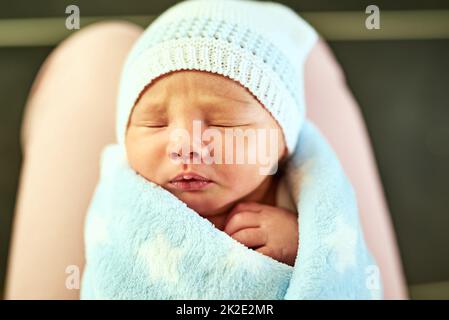 All wrapped up in a blanket and ready for bed. Shot of a tired little baby boy sleeping with his eyes closed while his mother holds him in her hands at home. Stock Photo