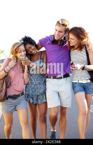 I love this song, dont you. Four friends sharing their music while walking down the street. Stock Photo