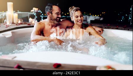 Celebrating our love the best way we know how. Shot of an affectionate mature couple relaxing in a hot tub together at night. Stock Photo