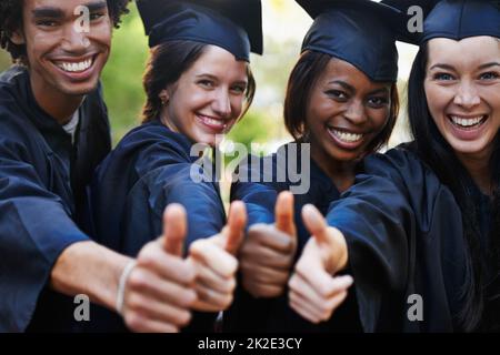 Get educated. A group of smiling college graduates giving the thumbs up at graduation. Stock Photo