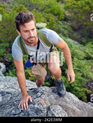 Heading in the right direction. Shot of a handsome young man scaling a mountain. Stock Photo