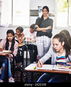 You can trust me with your childs education. Portrait of an attractive young teacher standing with her arms folded in a classroom. Stock Photo