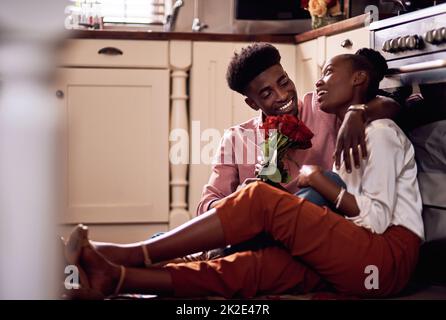 Every beautiful rose I see reminds me of you. Full length shot of an affectionate young man giving his wife a bunch of roses in their kitchen at home. Stock Photo