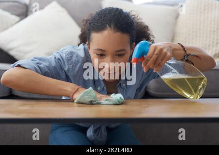 The wooden table is gleaming. Shot of a young woman wiping down her wooden coffee table in her living room at home. Stock Photo