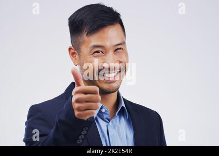 Great job. Studio portrait of a handsome young businessman giving a thumbs up against a grey background. Stock Photo