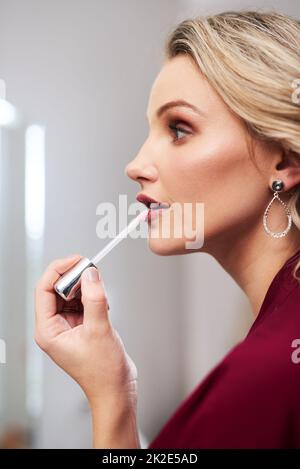 She definitely rocks this lip colour. Cropped shot of a beautiful young bride applying lipstick while preparing for her wedding in her dressing room. Stock Photo