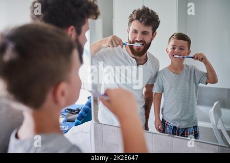 Start good oral habits early. Shot of a father and his little son brushing their teeth together in the bathroom at home. Stock Photo