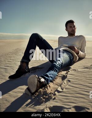 Stylish no matter where he is.... Full length of a handsome male model lying on the desert sand. Stock Photo