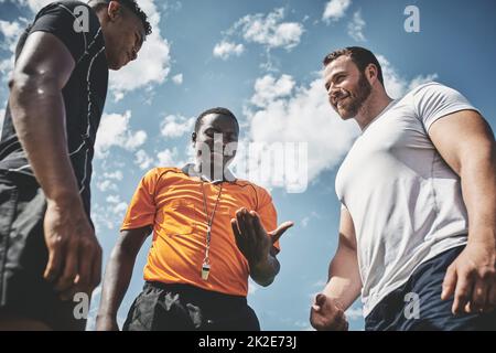 Lets see what the result is. Low angle shot a referee flipping a coin among two rugby team captains to see who will start the kickoff of the match outside during the day. Stock Photo