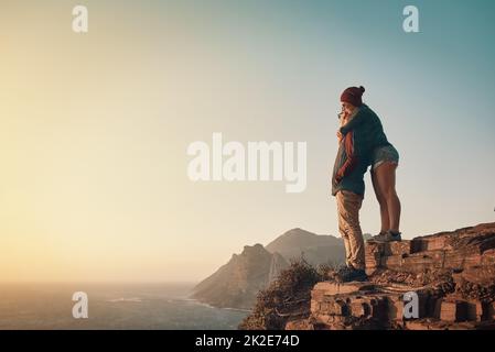 This view is incredible. Full length shot of an affectionate young couple taking in the view from a mountaintop. Stock Photo