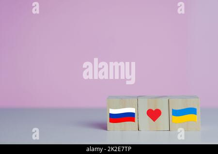 Wooden cubes with russia flag symbol and ukraine flag with red heart icon on background. Stock Photo