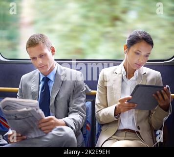 Optimizing their travel time wisely. Two business people reading catching up on the news on their commute to work. Stock Photo