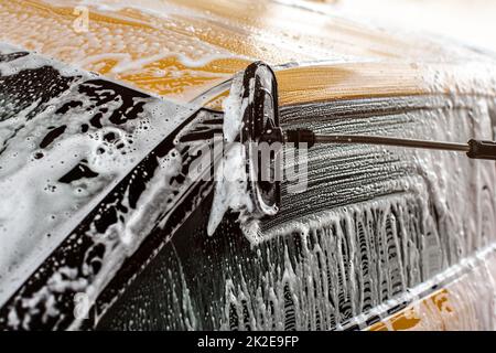 Side of yellow car being washed in self serve carwash, Brush leaving strokes on glass in shampoo and foam. Stock Photo