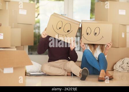 Having fun on moving day. Shot of a young couple on moving day wearing boxes with smiley face drawn on them on their heads. Stock Photo