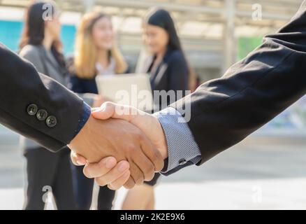 Two business men shaking hands in front of theirs business team standing outdoors. Stock Photo