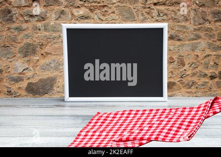 Food recipe template. Empty black board on a table with red checkered cloth against red brown concrete wall. For your food product placement or montage. Copy space. Stock Photo