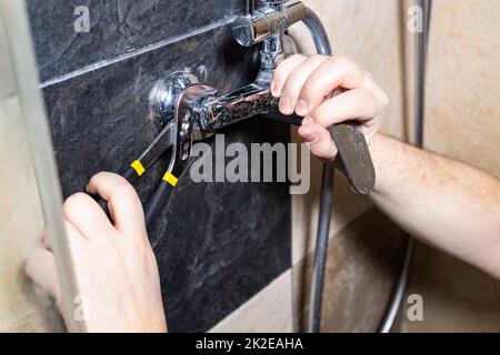 plumber installs shower faucet on tiled wall Stock Photo
